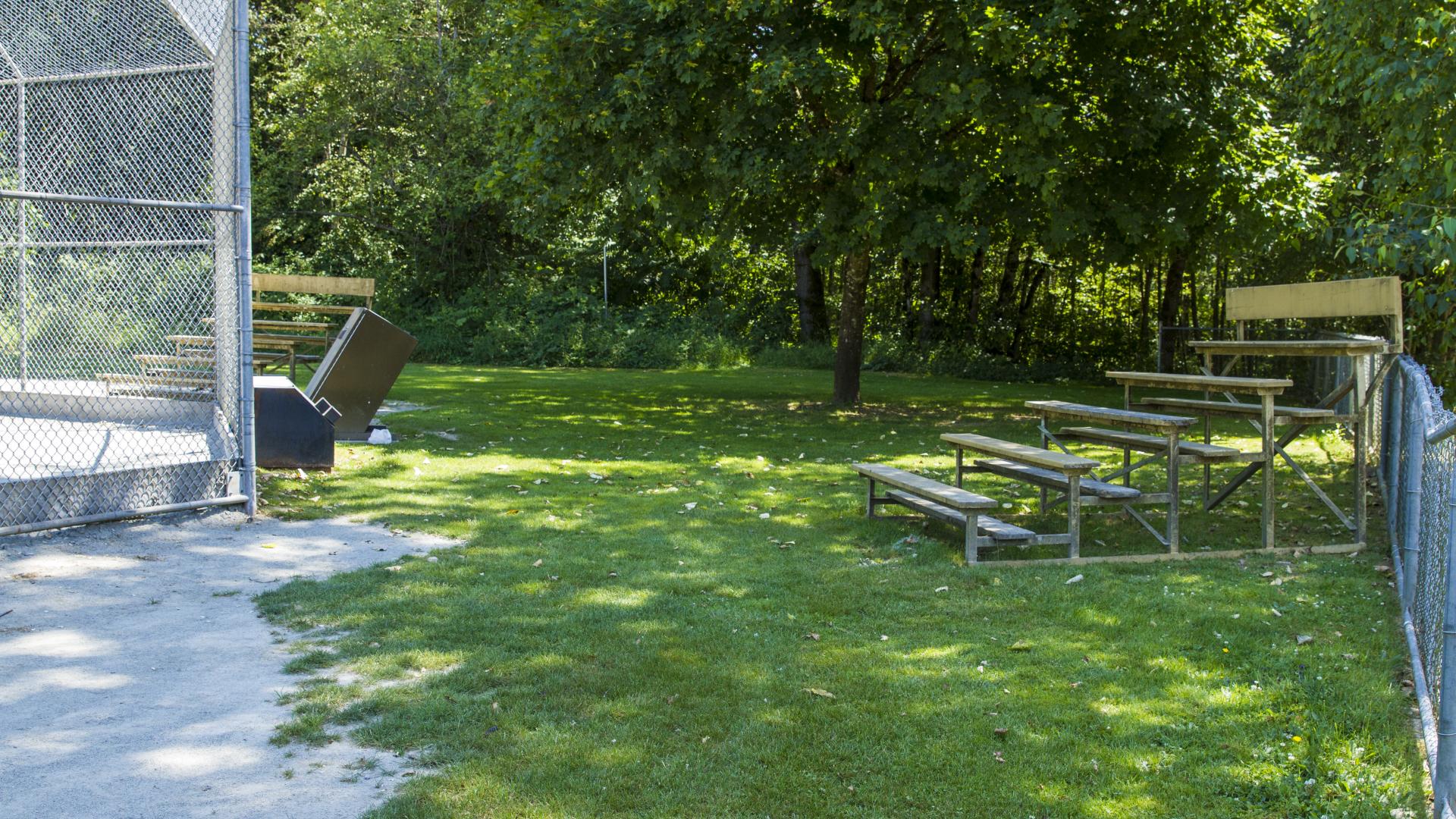 In the shade next to a baseball field sits a small set of bleachers.